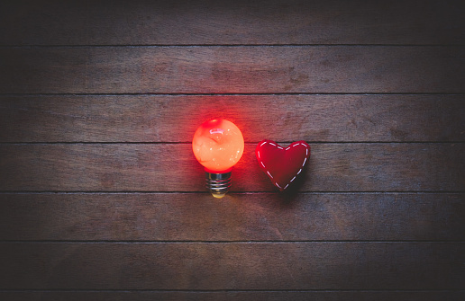 Heart shape toy and light on bulbs on wooden background
