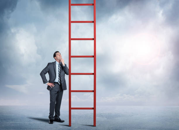 istock Businessman Looks Up At Red Ladder Extending Into The Clouds 881814840