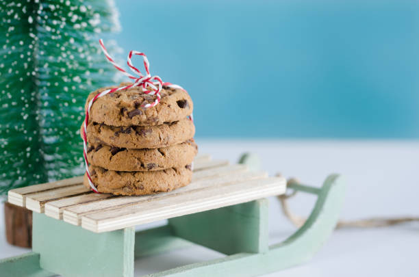 Wooden sled with chocolate biscuits and Christmas tree with blue background.