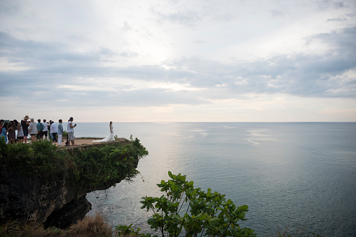Balangan Beach, Bali, Indonesia - March 16, 2017: A group of tourists, including a photographer and Chinese bride posing for wedding pictures, stand on an overlook at Balangan Beach in Bali.
