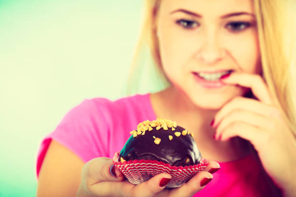 istock Cute blonde woman thinking about eating cupcake 881853374