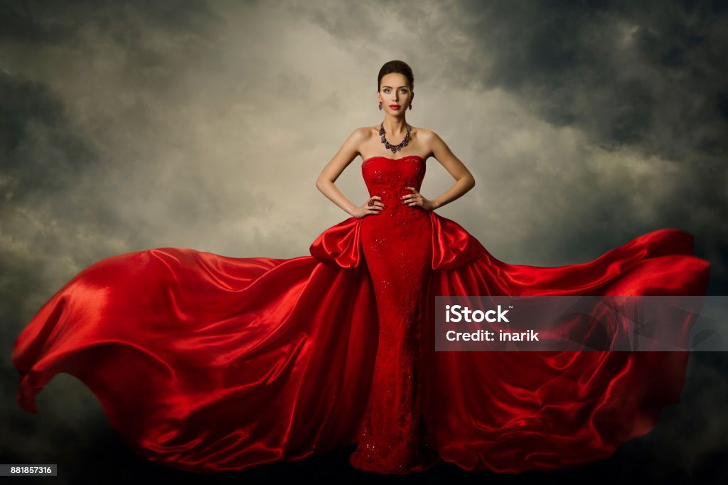 Fashion Model Art Dress, Elegant Woman in Red Retro Gown, Silk Fabric Fluttering in Storm Fashion Model Art Dress, Elegant Woman Standing in Red Retro Gown, Silk Fabric Fluttering over Storm Sky Background Luxury Stock Photo