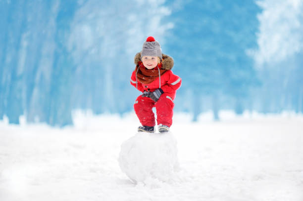 istock Little boy in red winter clothes having fun with snowball 881865868
