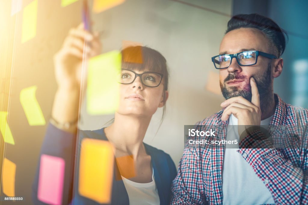 Young creative business people meeting at office. Business people meeting at office and use post it notes to share idea. Brainstorming concept. Sticky note on glass wall. Contemplation Stock Photo