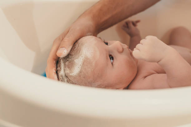 Hygiene and care for baby Hygiene and care for baby. Unrecognizable father bathing her son in white small plastic bat. Portrait of a baby is being bathed by his father using tub at home. Soft tone. Bath time for a cute little newborn baby young hot stock pictures, royalty-free photos & images