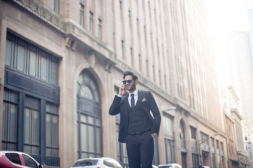 One man, elegant and modern, standing on the city street alone, talking on mobile phone.