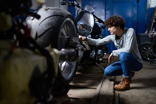 Concentrated skilled female mechanic creating custom motorcycles in garage and analyzing them before selling