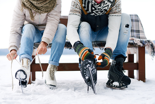 Unrecognizable couple sitting on bench and tying ice skates outdoors in winter
