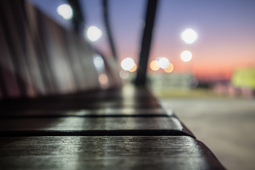 This is a close-up picture of a wooden bench taken in a city park at night.