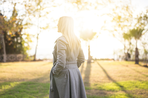 Side view of a young elegant woman walking in a park during sunset.