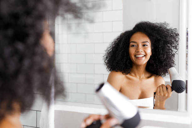 Smiling woman with hair dryer looking at mirror stock photo