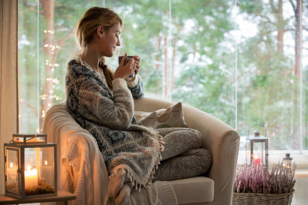 jeune femme assise à la maison par la fenêtre - home decorating photos photos et images de collection