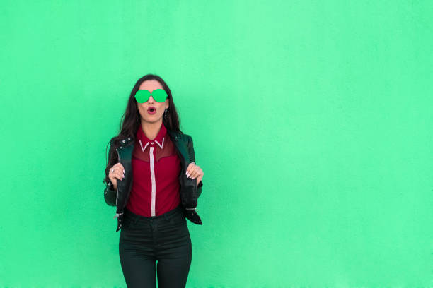 confident young woman with colorful glasses on green background - funky contemporary casual sex symbol imagens e fotografias de stock