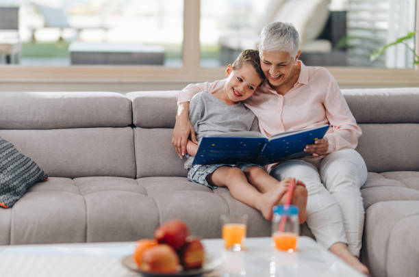 grand-mère adorée lire un livre à son petit-fils à la maison. - grandparent family reading inside of photos et images de collection