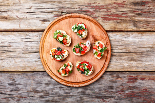 bruschetta italiana con tomates asados, queso mozzarella y hierbas sobre una tabla de cortar - bruschetta cutting board italy olive oil fotografías e imágenes de stock