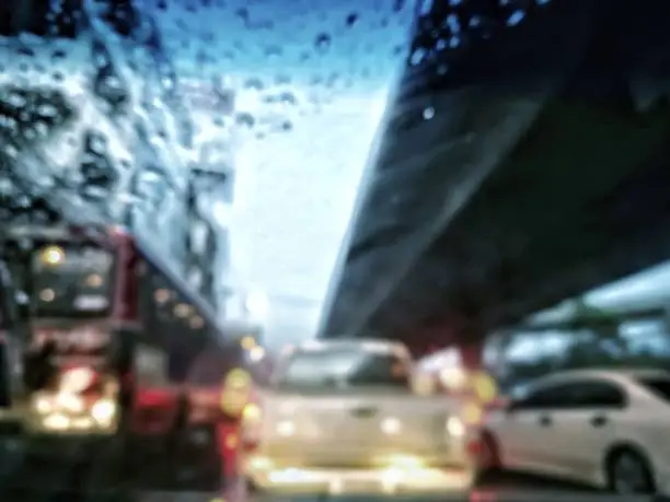 White pickup truck is at center, car beneath sky-train rail is on the right; red public bus is on the left; wet car glass from raindrops is foreground at top left corner.