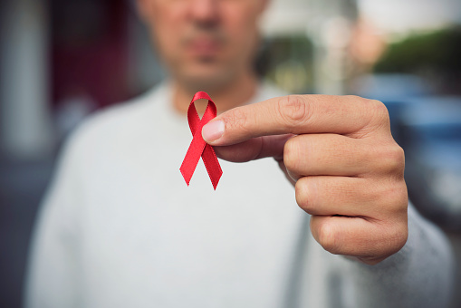 closeup of a young man with a red awareness ribbon for the fight against AIDS in his hand