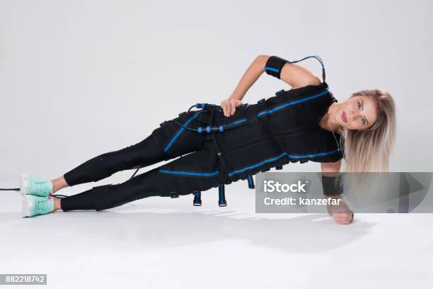 Beautiful Blonde In An Electric Muscular Suit For Stimulation Makes An Exercise On The Rug Stock Photo - Download Image Now