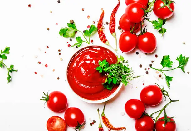 Tomato spicy ketchup sauce with cherry tomatoes in a bowl on white food background, top view