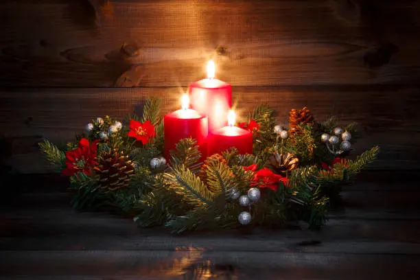Third Advent - Decorated Advent wreath with three red burning candles on a wooden background with festive atmosphere.