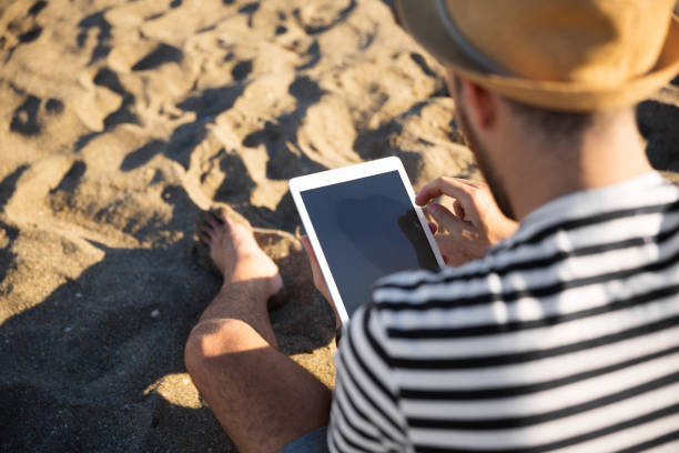 istock Back portrait of man sitting on beach using tablet 882229408