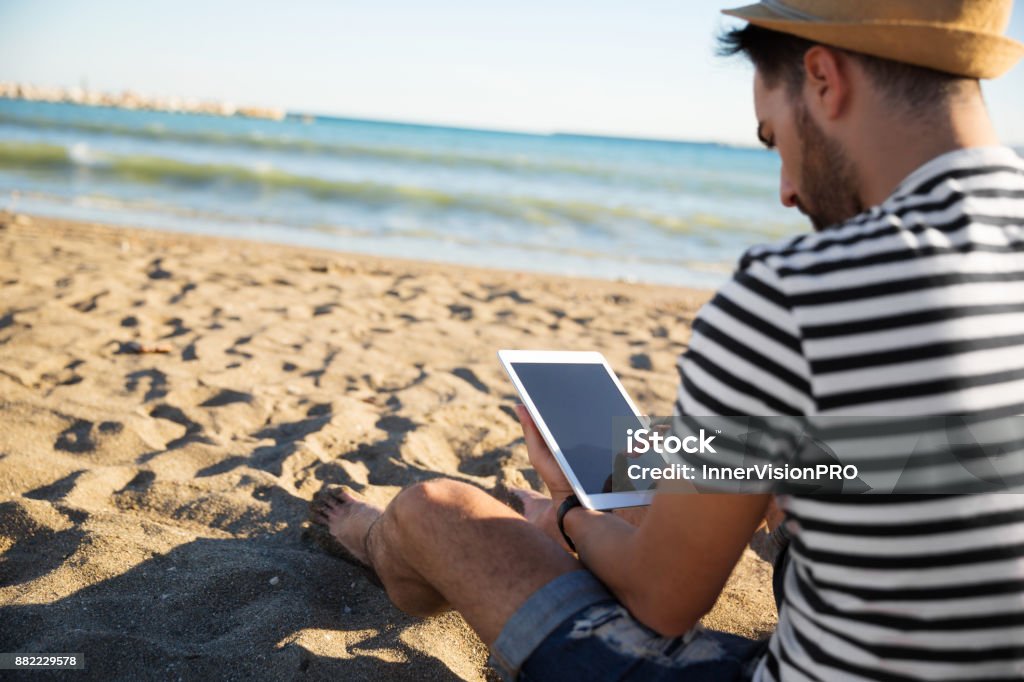 Hombre sentado en la playa leyendo ebook - Foto de stock de Tableta digital libre de derechos