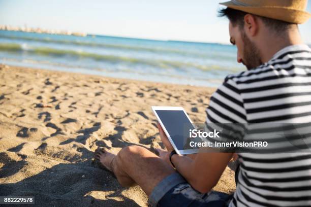 Hombre Sentado En La Playa Leyendo Ebook Foto de stock y más banco de imágenes de Tableta digital - Tableta digital, Playa, Verano