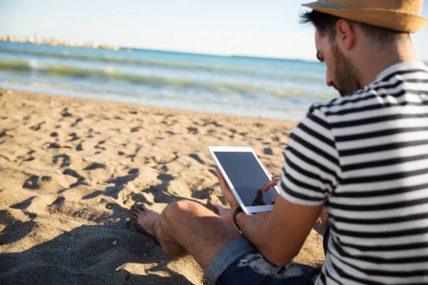 homme assis sur la plage de lecture ebook - reading beach e reader men photos et images de collection