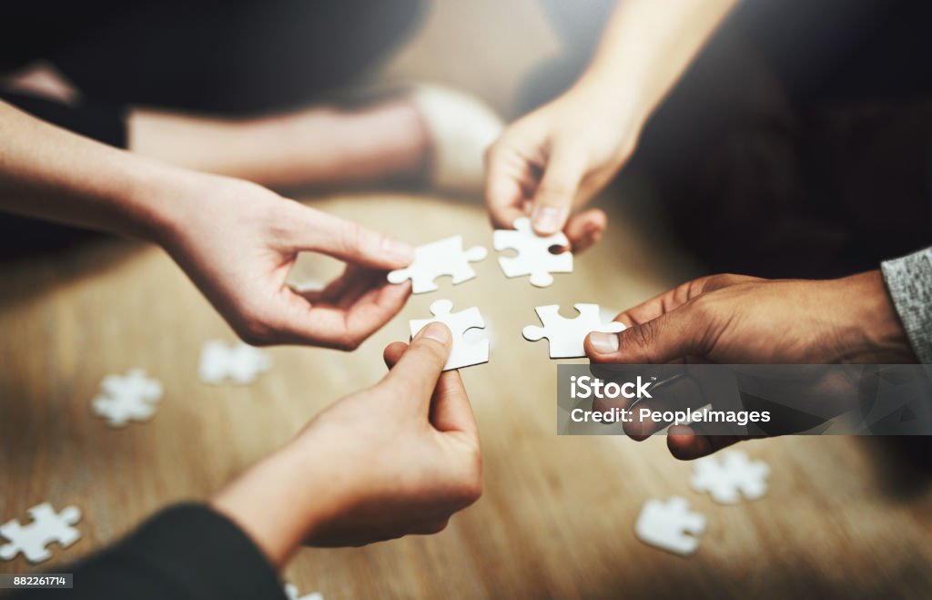 Pulling together to solve a problem Cropped shot of a group of unrecognizable people fitting puzzle pieces together on the floor Teamwork Stock Photo