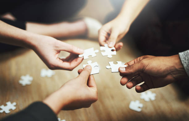 Pulling together to solve a problem Cropped shot of a group of unrecognizable people fitting puzzle pieces together on the floor coordination photos stock pictures, royalty-free photos & images