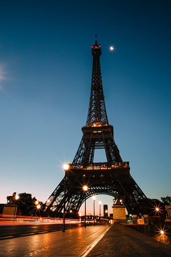 The Eiffel Tower over the green lawn field of Champ de Mars, Field of Mars, in Paris, France, an overcast sunset landscape