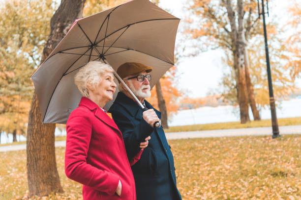 senior couple with umbrella in park - umbrella senior adult couple autumn imagens e fotografias de stock