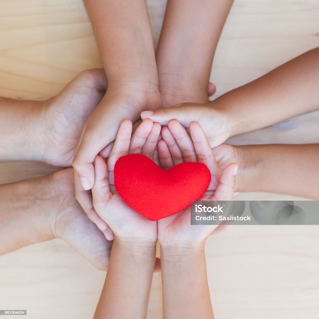 Red heart in parent and children holding hands together on wooden background Red heart in parent and children holding hands together on wooden background. Family and friend stack hands with red heart showing unity, teamwork and love Family Stock Photo