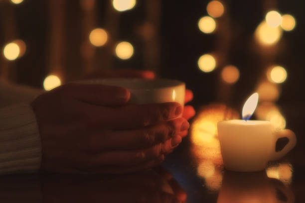 istock Woman hands holding tea cup on the table with burning candle. Special soft focus effect 882327588