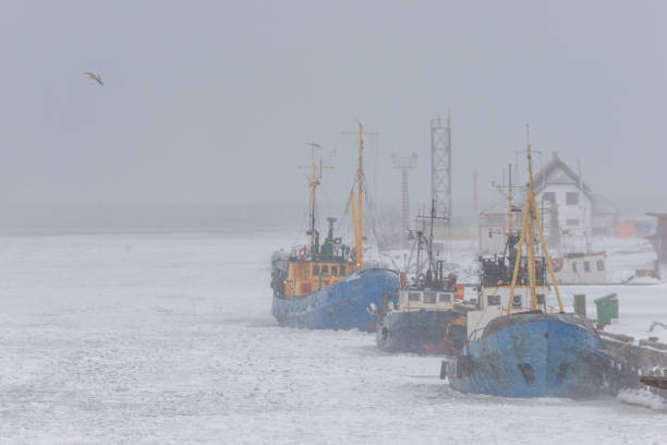 Ships of fishermen in the port on a frozen river in winter through a strong blizzard to the horizon
