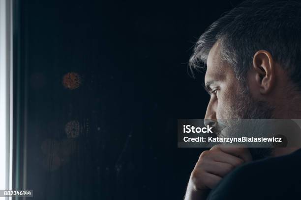 Man Holding Chin Beside Window Stock Photo - Download Image Now - Men, Contemplation, Depression - Sadness