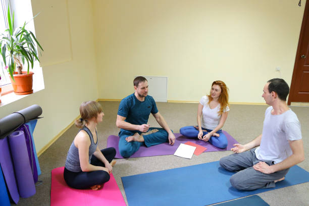 istock Four young people sit on floor on yoga mats and communicate 882357390