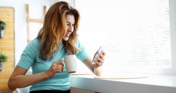 istock Beautiful woman using cell phone and drinking morning coffee 882362114