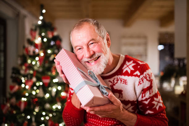 istock Senior man in front of Christmas tree holding a gift. 882389682