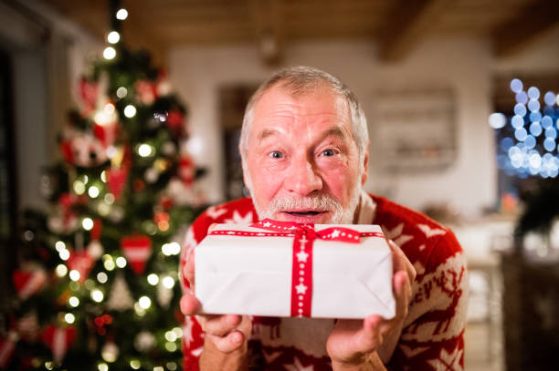 istock Senior man in front of Christmas tree holding a gift. 882389808