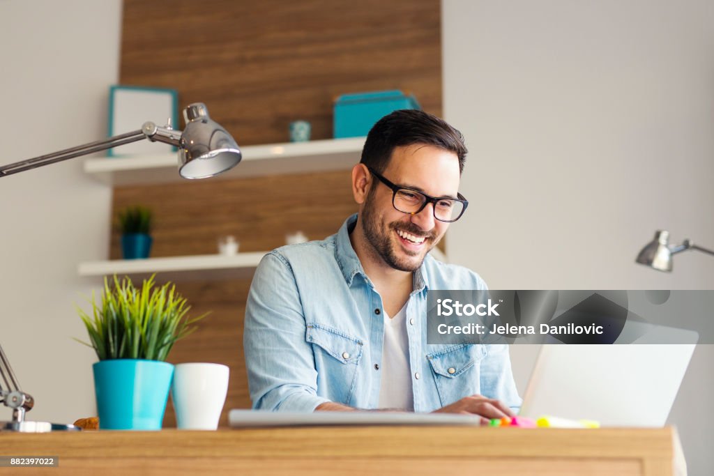 Remote job Smiling young freelancer typing on his laptop at the office Men Stock Photo