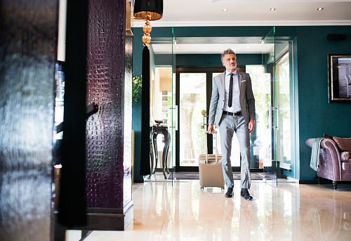 Mature businessman entering or leaving hotel with luggage. Man walking in the hotel entrance hall.