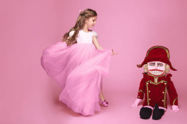 A young girl with blonde hair tied up in a ponytail, wearing a pink tutu, is captured mid-run on a green lawn. Her face is lit with a bright smile as she enjoys her playful moment outdoors. The backdrop of a lush garden and a charming house adds to the lively and vibrant scene, embodying the joy and freedom of childhood.