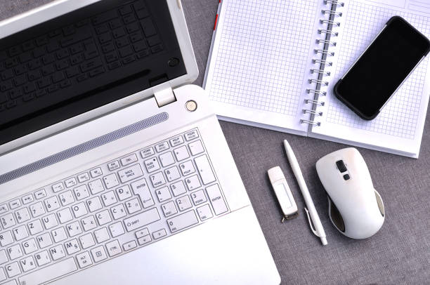 bem acima vista do escritório local de trabalho com telefone celular e laptop perto teclado de computador e mouse com caderno, caneta e usb flash na mesa cinza. conceito de mesa de mesa de trabalho - mobile office flash - fotografias e filmes do acervo