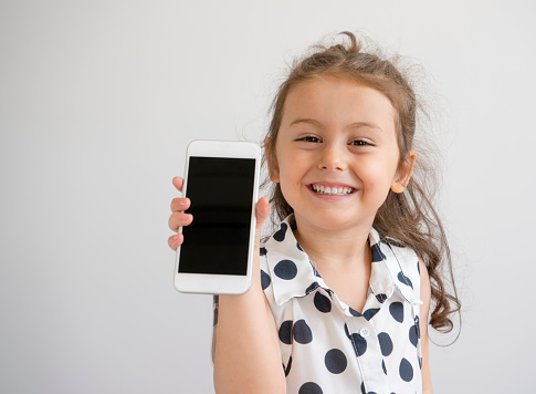 Cute little girl showing mobile phone screen, studio shot