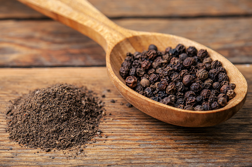 black pepper ground and grains on wooden background