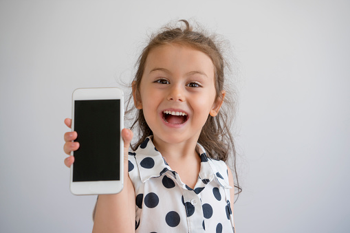 Cute little girl showing mobile phone screen, studio shot