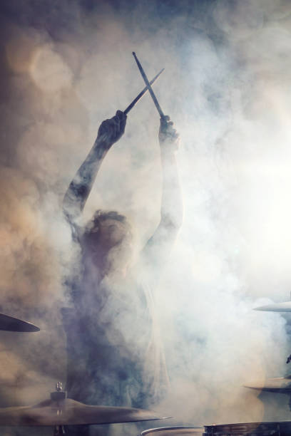 Drummer posing surrounded by fog Drummer in epic posture with crossed sticks surrounded by dense fog. drummer stock pictures, royalty-free photos & images