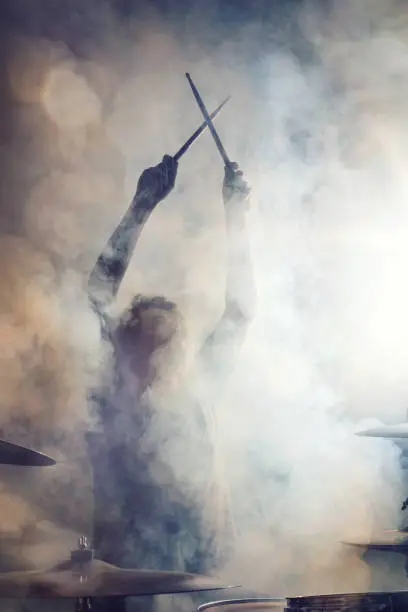 Drummer in epic posture with crossed sticks surrounded by dense fog.