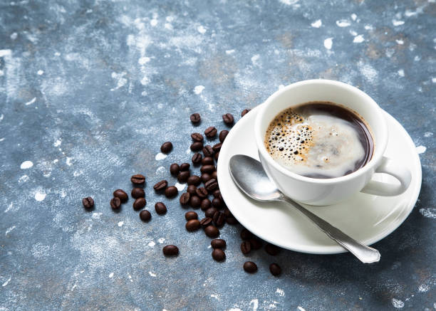 Cup of coffee on a table and beans scattered around.